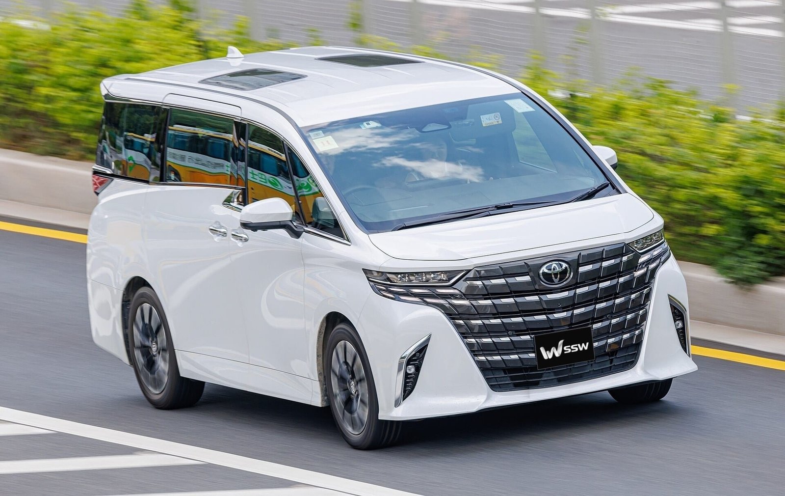 White Toyota Alphard (AH40) in front three-quarter view in daylight, with a motion-blurred background