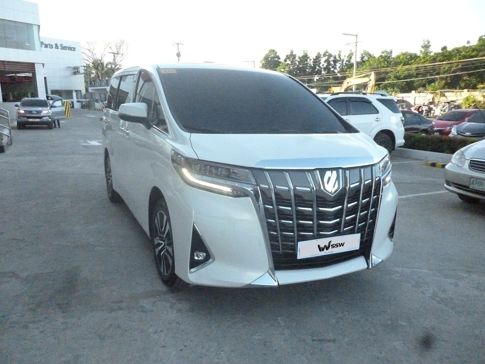 White Toyota Alphard 3.5 V6 (AH30), front three-quarter view on a Toyota dealership forecourt in Nueva Ecija, Philippines