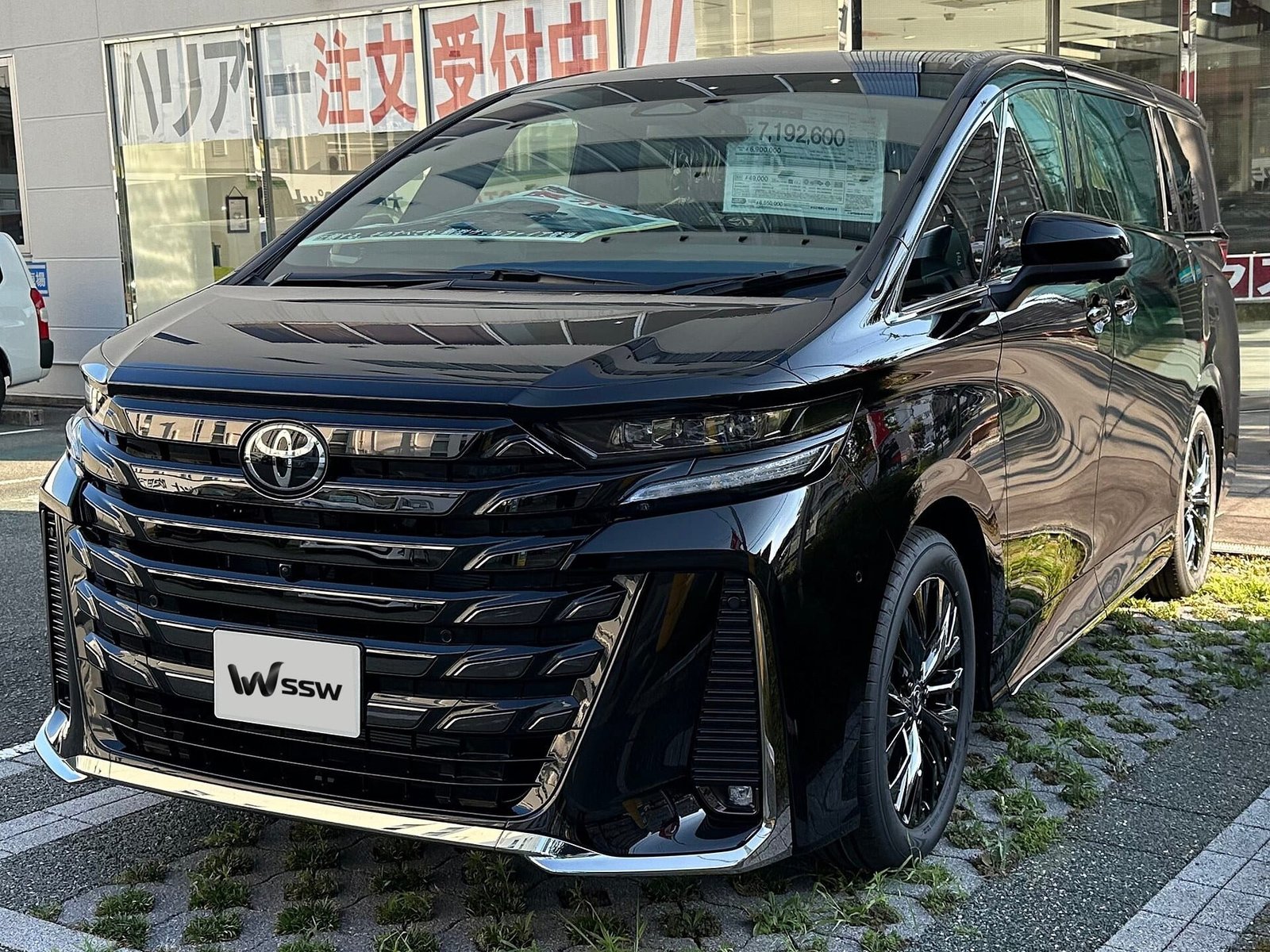 Black Toyota Vellfire (AH40) in front three-quarter view on a dealership lot in Japan, in daylight